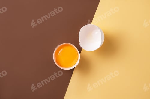 Preview: a fresh egg broken into two halves on a yellow and brown background