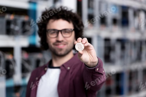 Preview: handsome computer engineer holding bitcoin at cryptocurrency mining farm