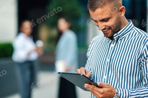 Preview: Young businessman using digital tablet outside of office building