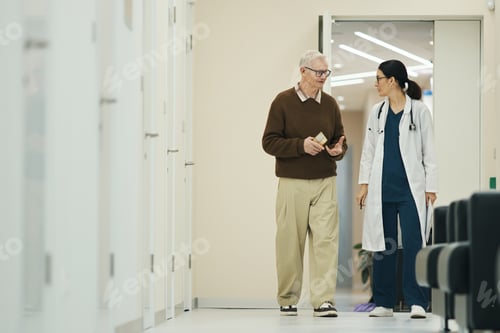 Preview: Senior Man Walking with Female Doctor in Hospital Corridor