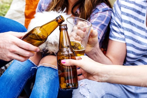 Preview: Selective focus shot of the group of friends clinking bottles of beer