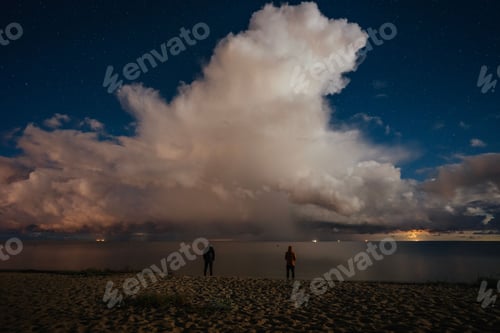 Preview: Long exposure of a lake and two people standing on the shore before clouds and sky