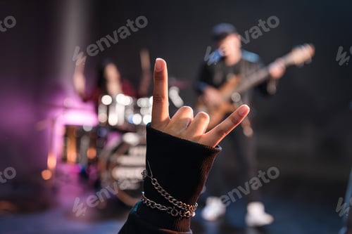 Preview: Person showing sign of the horns while rock band playing on stage