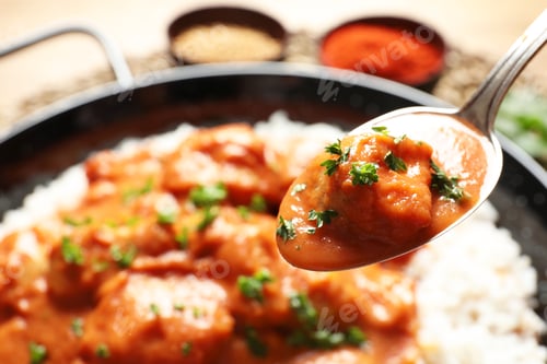 Preview: Tasty butter chicken in spoon over dish with meal, closeup