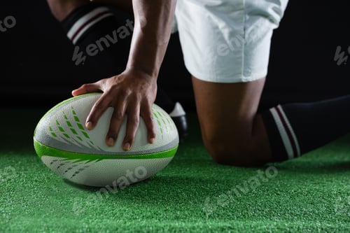 Preview: Side view of sportsman kneeling while holding rugby ball