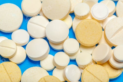 Preview: Different types of round and oval tablets scattered on a blue surface