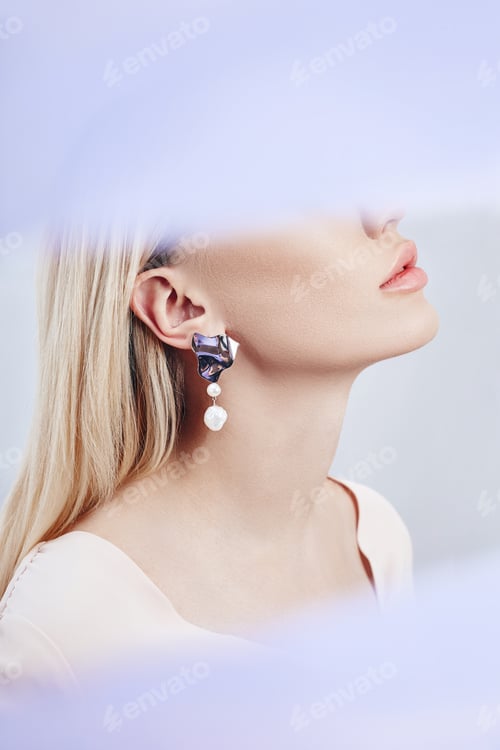 Preview: Earrings and jewelry in ear of a sexy blonde woman through a transparent colored fabric