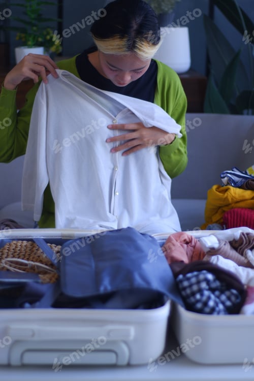 Preview: Young Asian women folding clothes, packing luggage for holiday trip.