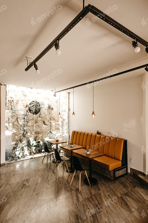 Preview: Vertical shot of a cafe interior with an orange sofa, three tables, and three black chairs