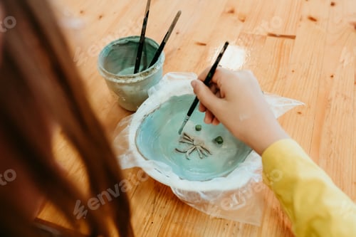 Preview: Girl painting handmade ceramic plate working with clay at ceramic workshop. Creative activity