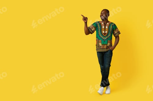 Preview: Cheerful black man in traditional shirt pointing at copy space