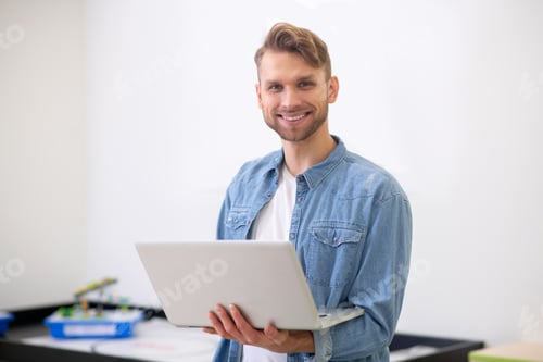 Preview: Male teacher standing, holding laptop and smiling