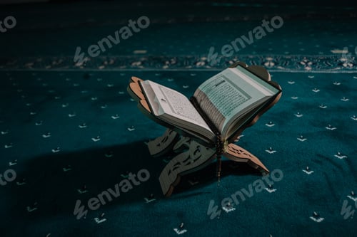 Preview: Closeup of an opened holy book of Quran put on a wooden pedestal on a carpet