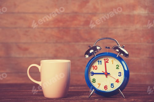 Preview: Cup of coffee and alarm clock on wooden table.