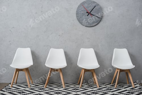 Preview: Row of empty white chairs in a waiting room at company with wall clock