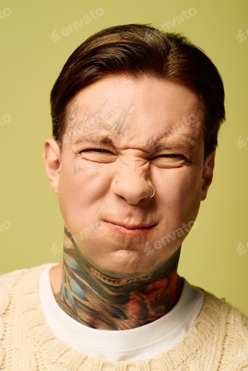 Preview: A young man with vibrant tattoos makes a playful expression against a solid color backdrop