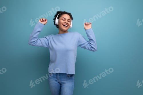 Preview: energetic 20s young afro brunette woman with wireless headphones on studio background with copy
