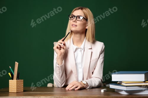 Preview: Portrait of beautiful teacher sitting at table near chalkboard