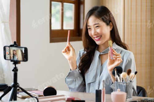 Preview: Beauty blogger reviewing lipstick product while recording video on smartphone for makeup vlogger