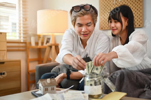 Preview: Happy young Asian couple putting money into savings jars and planning retirement finances