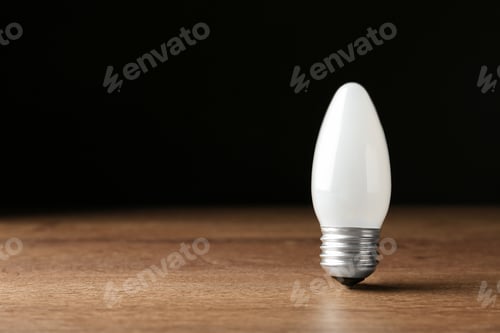 Preview: New modern lamp bulb on wooden table against black background. Space for text