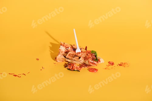 Preview: close up view of disposable fork in smashed piece of pizza on orange backdrop