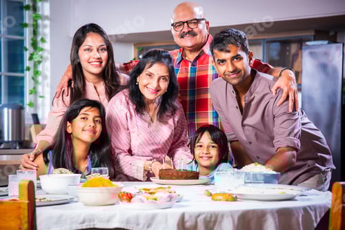 Preview: Indian asian grandparents with Family celebrating birthday by blowing candles on cake at home