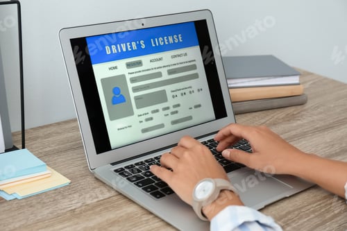 Preview: Woman using laptop to fill driver's license application form at table in office, closeup
