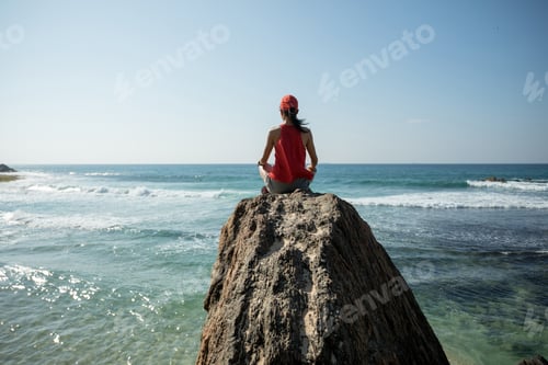 Preview: Young yoga woman meditating on seaside rock cliff edge