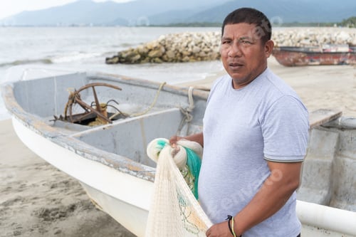 Preview: Fisherman holding net standing by boat on beach