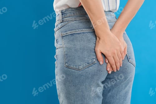Preview: Woman suffering from hemorrhoid on light blue background, closeup