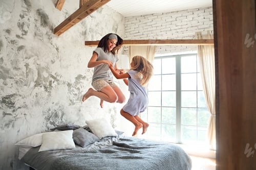 Vista previa: Una joven feliz y su pequeña y linda hija se divierten en la cama mientras están juntas en casa