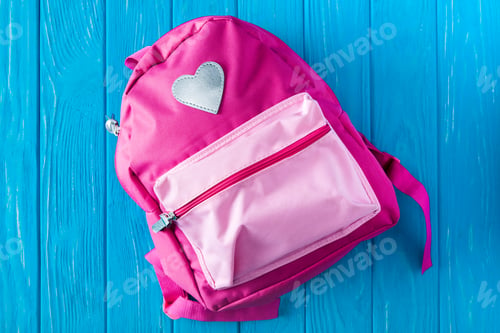 Preview: top view of pink backpack on blue wooden background