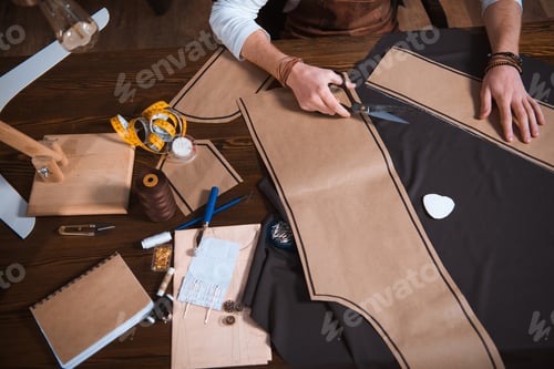 Preview: cropped shot of male fashion designer working with sewing patterns, tools and fabric at workplace