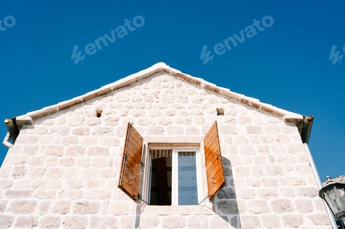 Preview: Open wide wooden shutters of the attic window of an ancient stone house