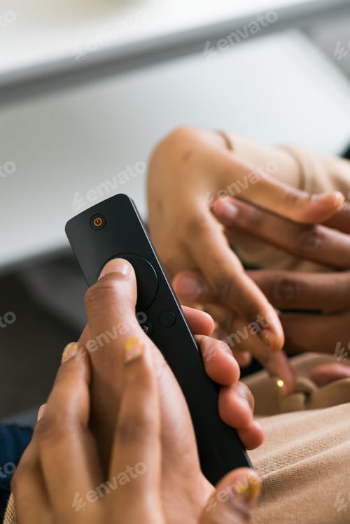 Preview: Hand holds a remote control while a bowl of popcorn sits on a white table in a modern living room