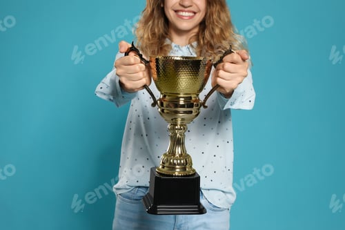 Preview: Young woman with gold trophy cup on blue background, closeup