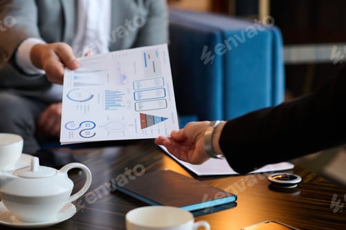 Preview: Close-up of financial document being passed by analyst to colleague