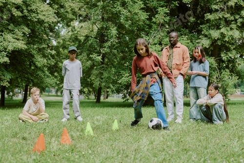 Preview: Multiethnic Children and Young Adult Teacher Playing Soccer in Park Outdoors