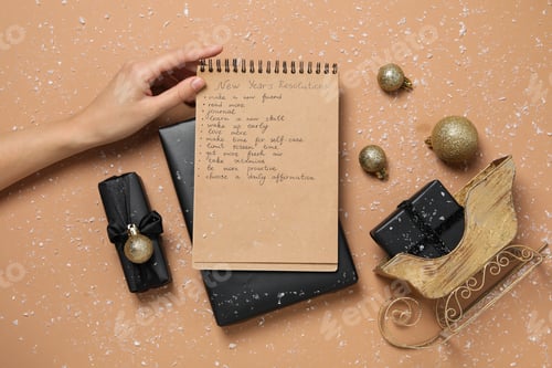 Preview: Gift boxes, decorations and notepad with list in hand on beige background, top view