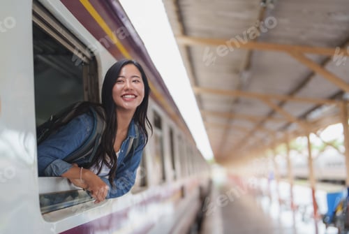 Preview: Young tourist smiling and leaning out of train window at station