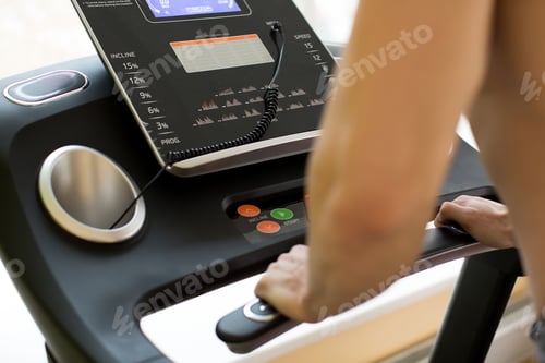 Preview: Young man athlete exercising on treadmill in modern gym, setting up difficulty level.