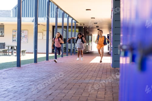 Preview: Three biracial girls are running joyfully down a school corridor with copy space