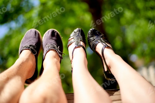 Preview: Four legs wearing shoes are extended against a blurred background of lush green foliage.