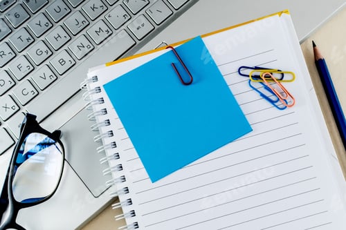 Preview: Top view of colorful paper clips on a blank notepad on a laptop
