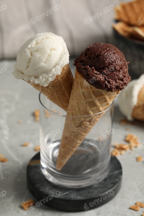 Preview: Tasty ice cream scoops in waffle cones on grey marble table, closeup