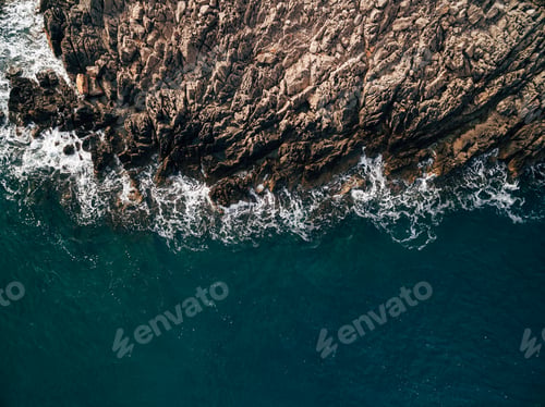 Preview: Top view of the blue sea with waves beating on beach and rocks.