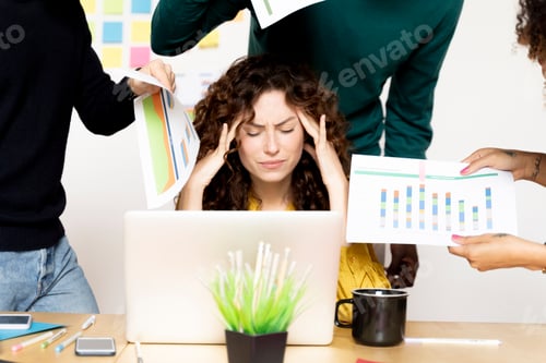 Preview: Stressed woman siting at desk in office surrounded by colleagues