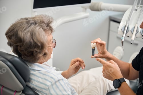 Preview: Doctor shows a model of dental implant to elderly lady