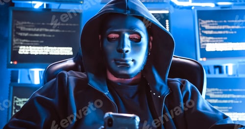 Preview: A hacker wearing a mask to cover his face is using computer to hack data to get ransom from victims.
